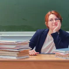 Nauczycielka zamyślona nad stertą prac, czekając na podwyżki dla nauczycieli 2026.