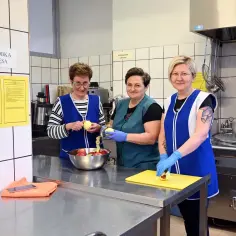 Trzy kobiety w fartuchach obierają jabłka w kuchni. Pracują w zespole, przygotowując posiłek. To praca dla dobrego intendent.
