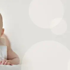 Uśmiechnięte, 4 miesięczne dziecko z szeroko otwartymi oczami i buzią leży na brzuchu.