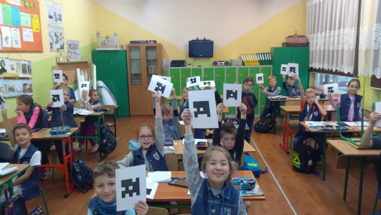 Dzieci w klasie trzymają karty z symbolami. Ich zaangażowanie to charakterystyka lekcji z nowoczesnymi technologiami.