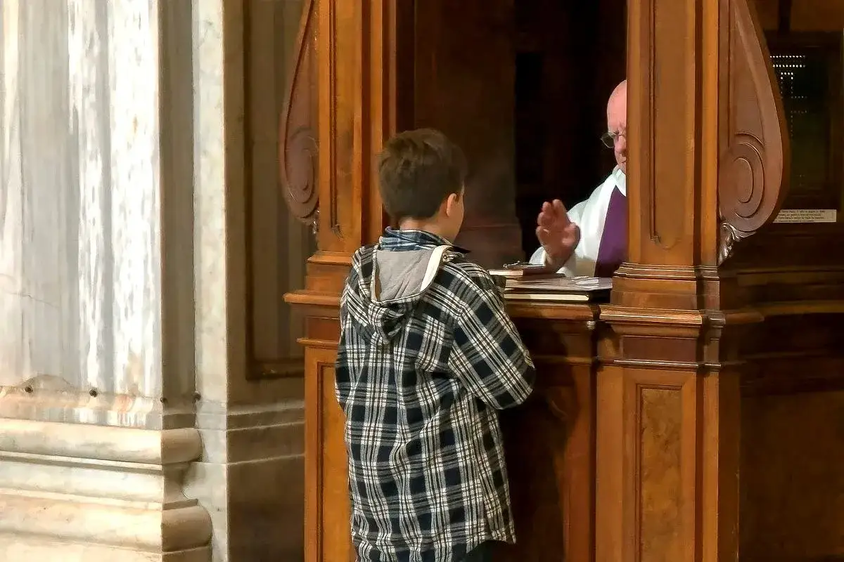 Chłopiec w kratkę słucha księdza w konfesjonale. To ważny moment, jak formuła spowiedzi dla dzieci.