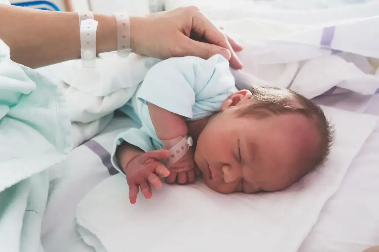 Dłoń matki głaszcze śpiące dziecko z opaską na nadgarstku, które może mieć cytomegalię u noworodka.