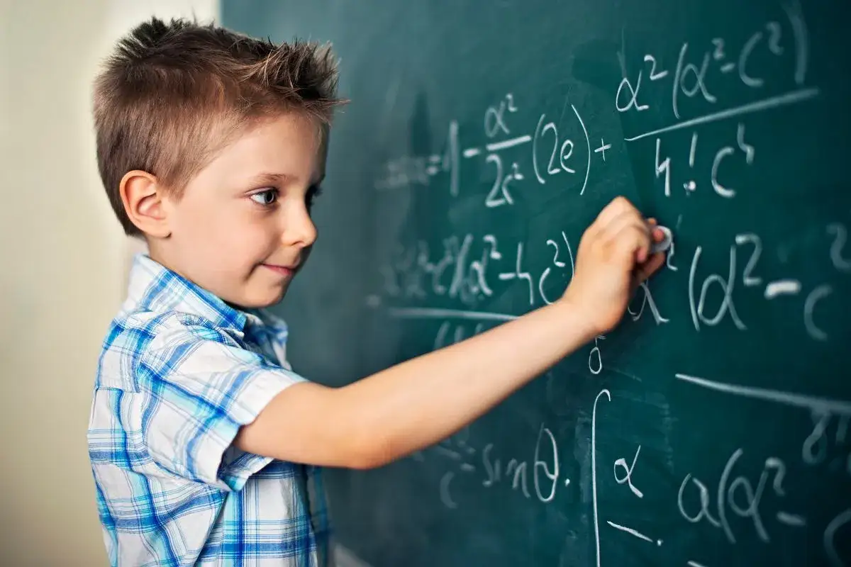 Chłopiec pisze kredą po tablicy skomplikowane wzory matematyczne. Zastanawia się, co to jest różnica między tymi równaniami.