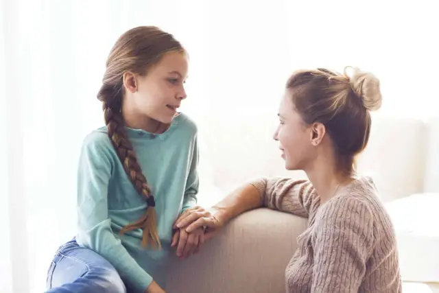 Mama rozmawia z córką o jej pierwszym okresie. Dziewczynka ma warkocz, a mama upięte włosy.